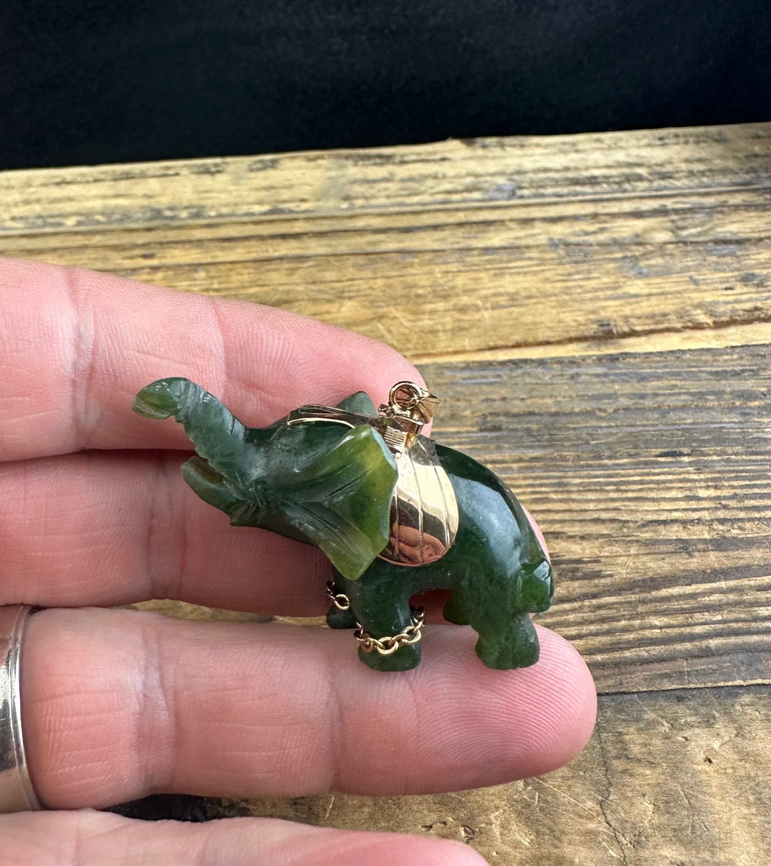 Hand holding the jade elephant pendant to reveal its carved green body and gold saddle.