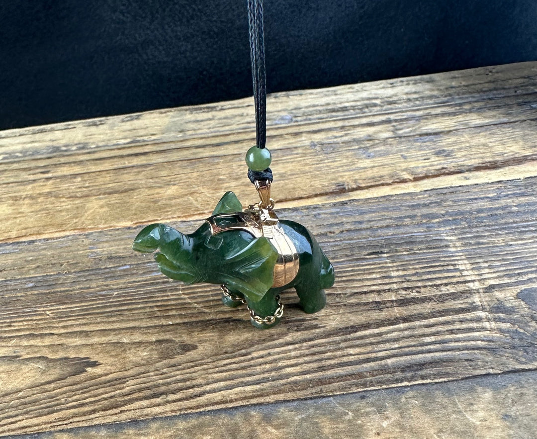 Vintage Jade Elephant Pendant hanging from a black cord with gold hardware on a weathered wood surface.