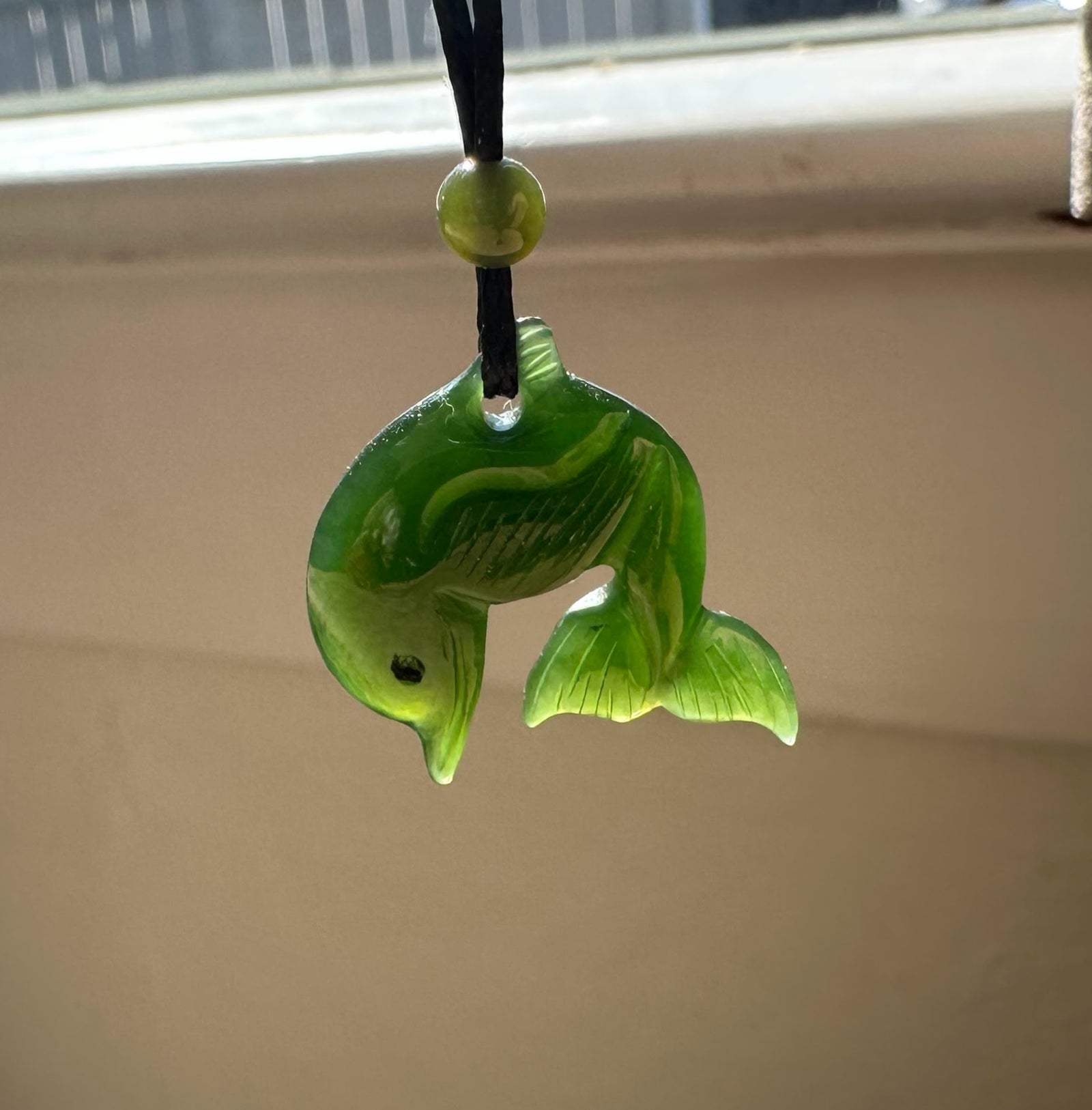 Glossy green jade dolphin pendant with a hole at the top, on a black cord with a green bead