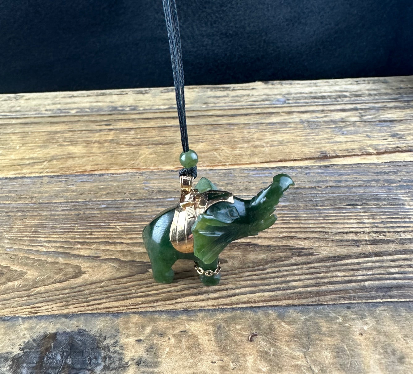 Jade elephant pendant on black cord necklace with a small green bead above the pendant