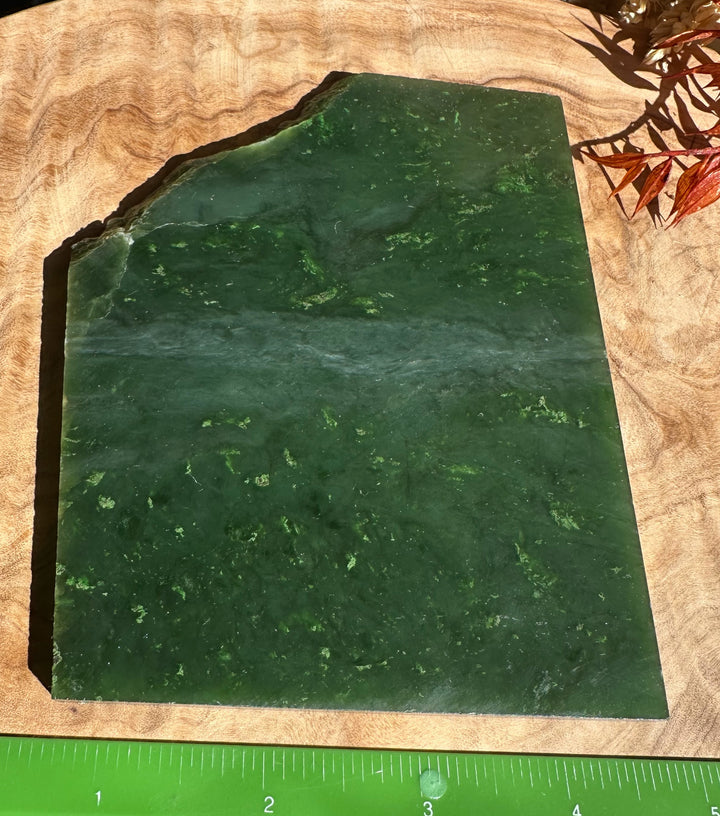 A Grade Canadian jade slab in dark green with an irregular top edge on a wooden surface.