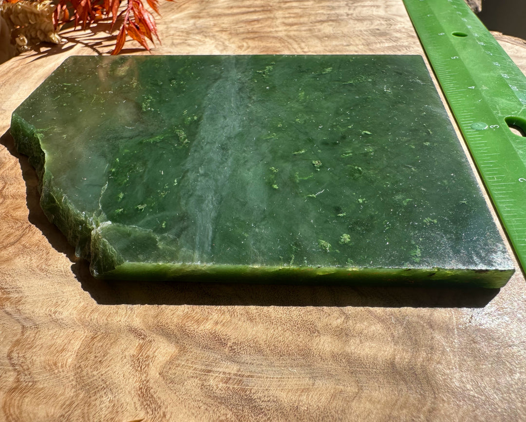 A Grade Canadian jade slab with a rough chipped left edge and visible thickness on a wooden surface.