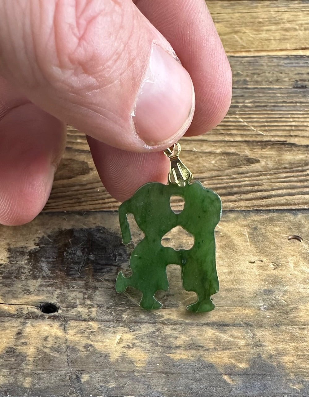 Green jade pendant carved into a stylized standing figure with cutouts and a gold bail