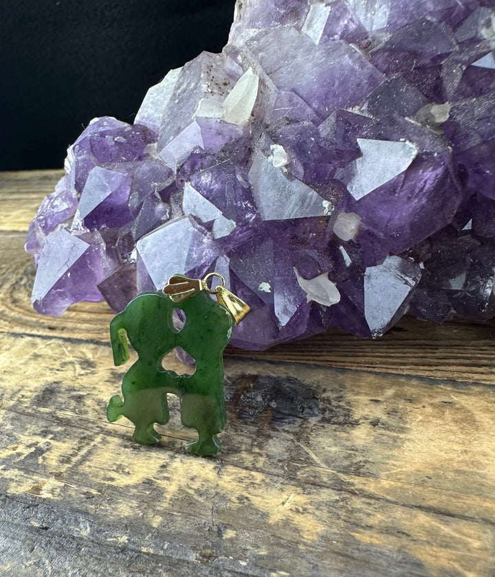 Green jade Young Love Pendant with gold bail seen from the side against a bed of amethyst crystals.