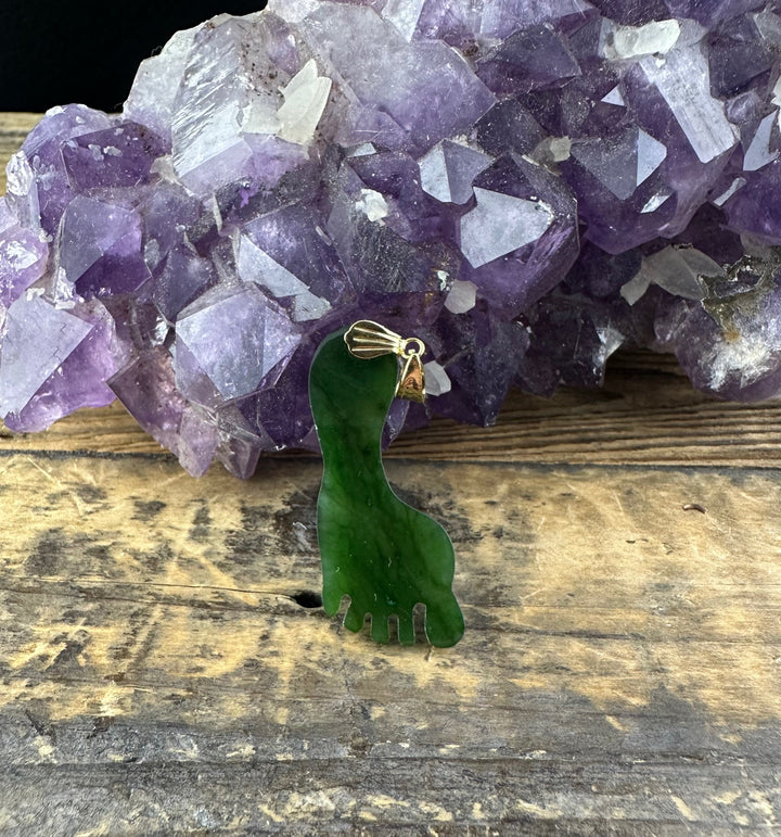 Close up of green jade Big Foot pendant with gold bail and chain draped over a purple amethyst cluster