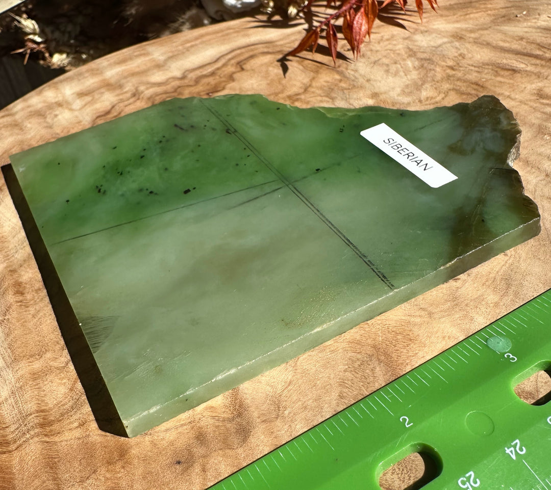 Green nephrite jade slab on a wood surface with a Siberian label and a ruler nearby