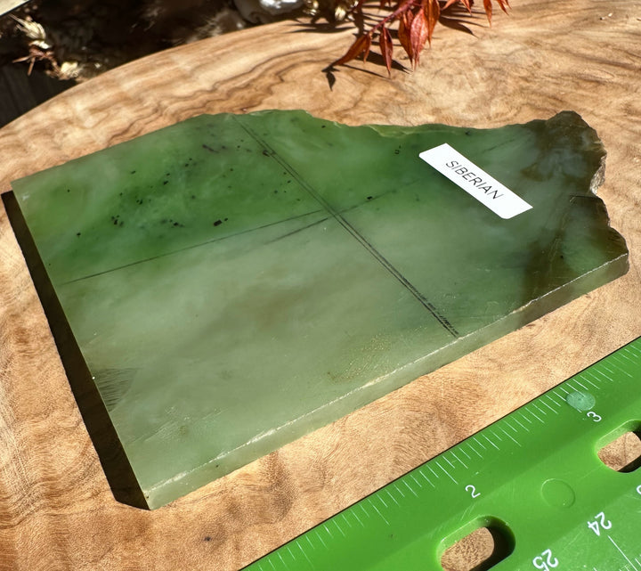 Green nephrite jade slab on a wood surface with a Siberian label and a ruler nearby