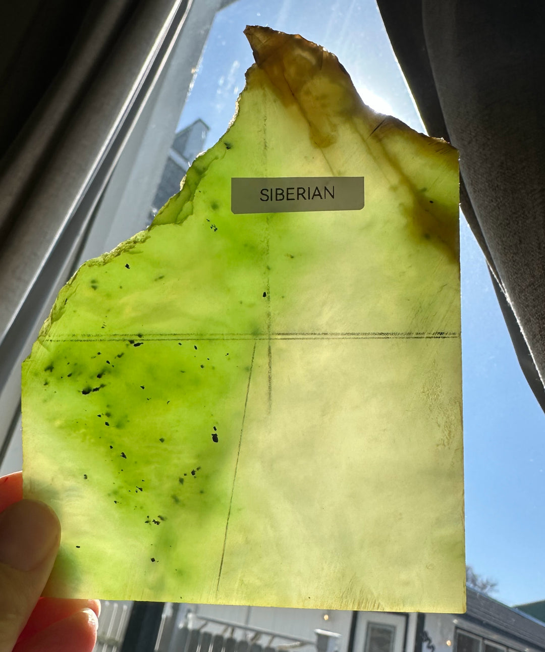 Rough-edged neon green nephrite jade slab with a Siberian label held against a window