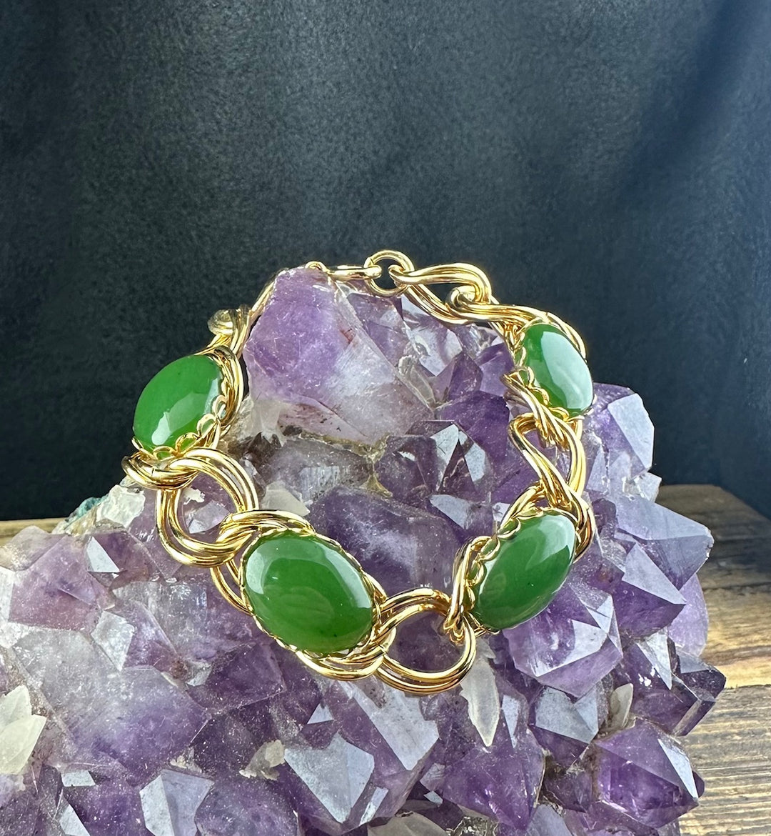 Gold chain bracelet with green jade cabochon beads arranged around a purple amethyst cluster