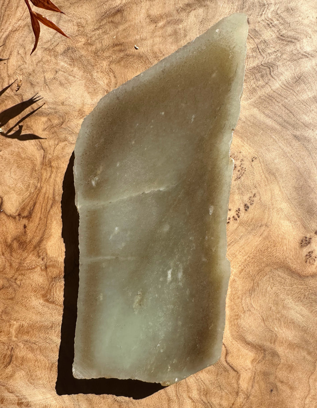 Siberian rough jade fragment with pale green translucent surface and rugged edges on wood