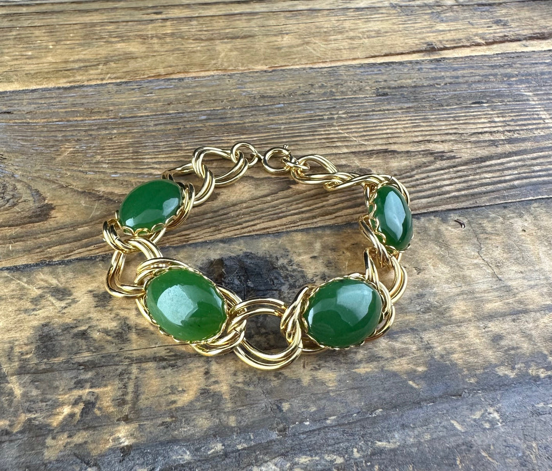 Gold twisted-link bracelet with green jade cabochons set between rounded links on wood.