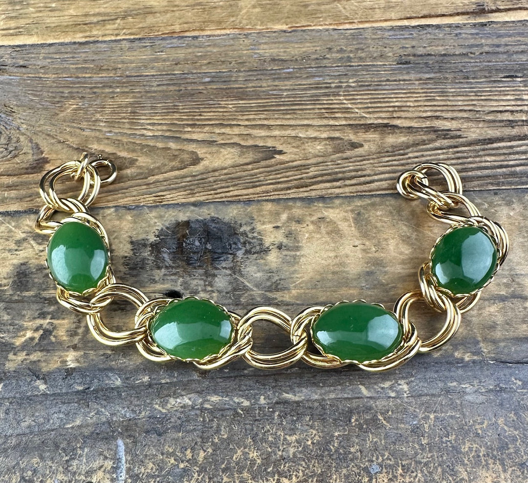 Gold tone bracelet with oval green jade cabochons linked by twisted wire on a rustic wooden surface.