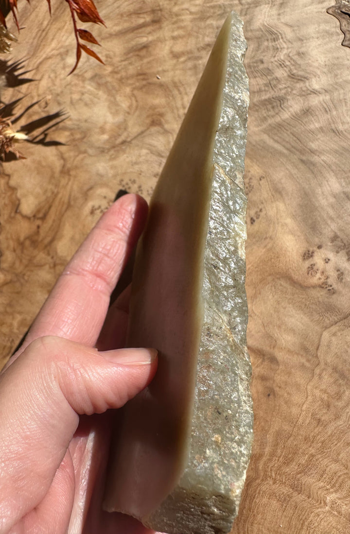 Siberian rough jade weighing 225 grams held in hand against a wooden background