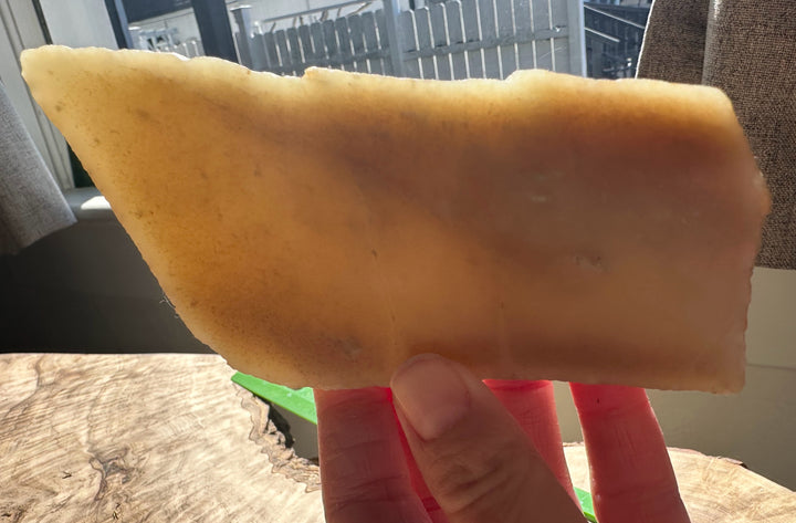 Pale yellow rough jade slab held between fingers outdoors