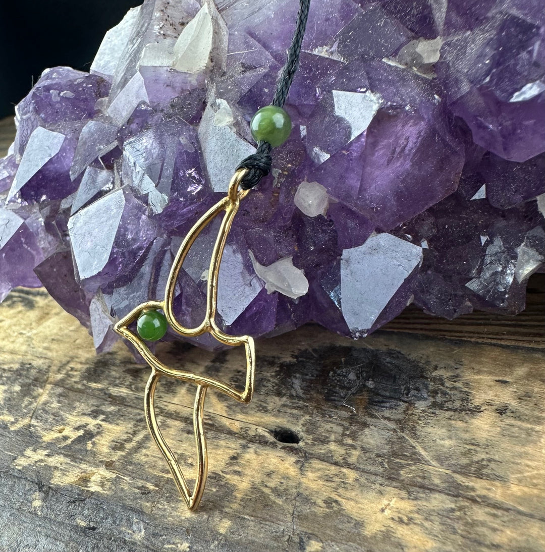 Vintage Jade and Brass Bird Pendant hanging from a black cord beside a purple amethyst cluster