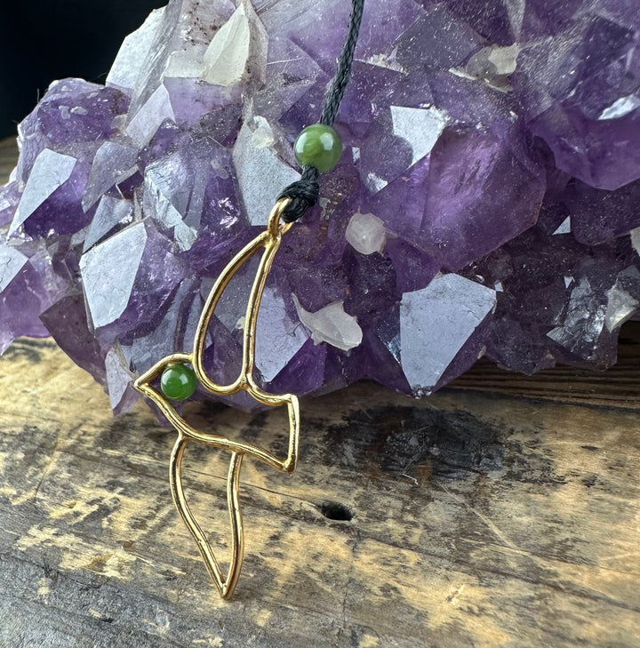 Vintage Jade and Brass Bird Pendant hanging from a black cord beside a purple amethyst cluster
