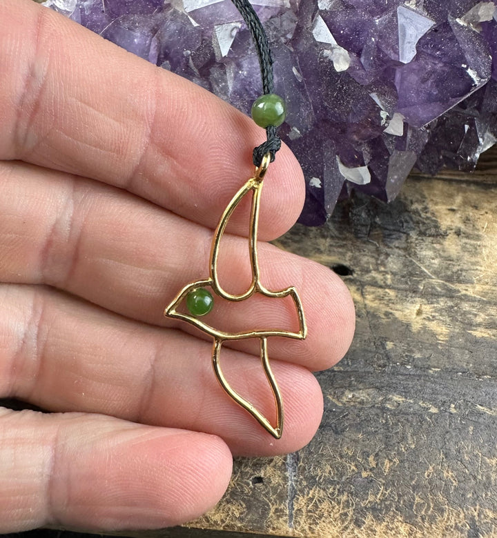 Close up of Vintage Jade and Brass Bird Pendant held between fingers against a wooden surface, showing a green bead eye