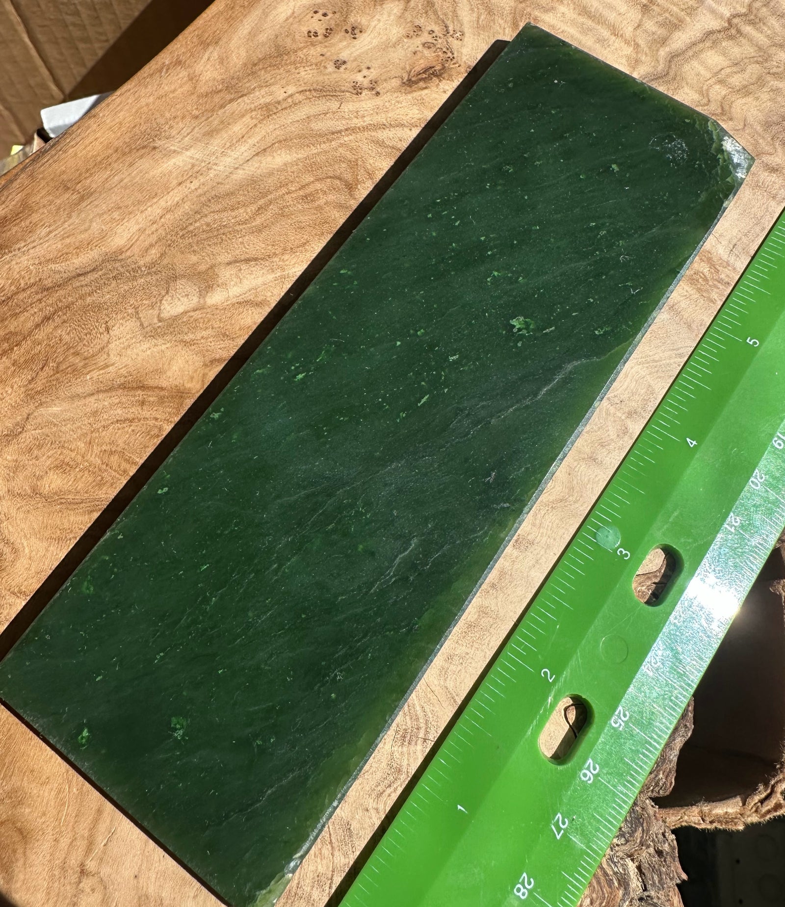 Dark green Canadian jade slab on a wooden surface with a green ruler for scale