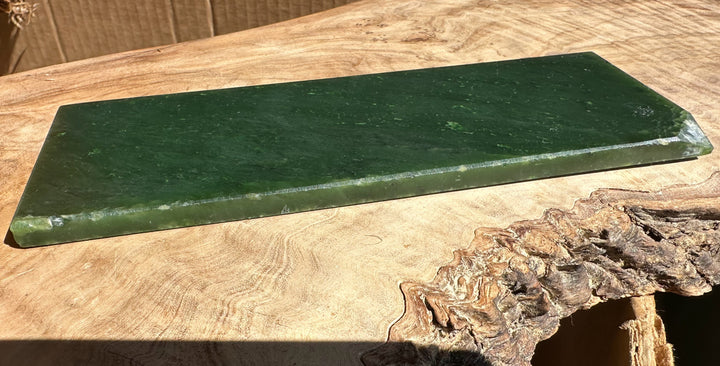 Long rectangular jade slab with a dark green surface on wood beside a measuring ruler for scale.
