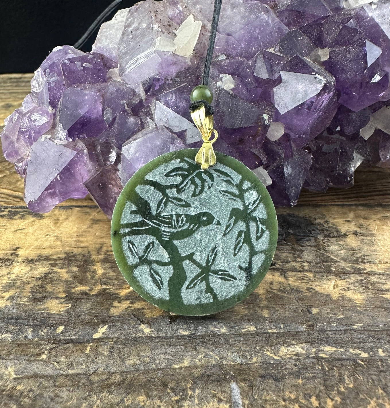 Round green jade bird pendant with a carved bird among branches hanging from a cord.