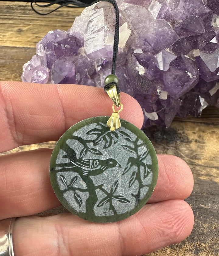 Vintage green jade disc pendant engraved with a bird among leaves, gold bail, on a black cord