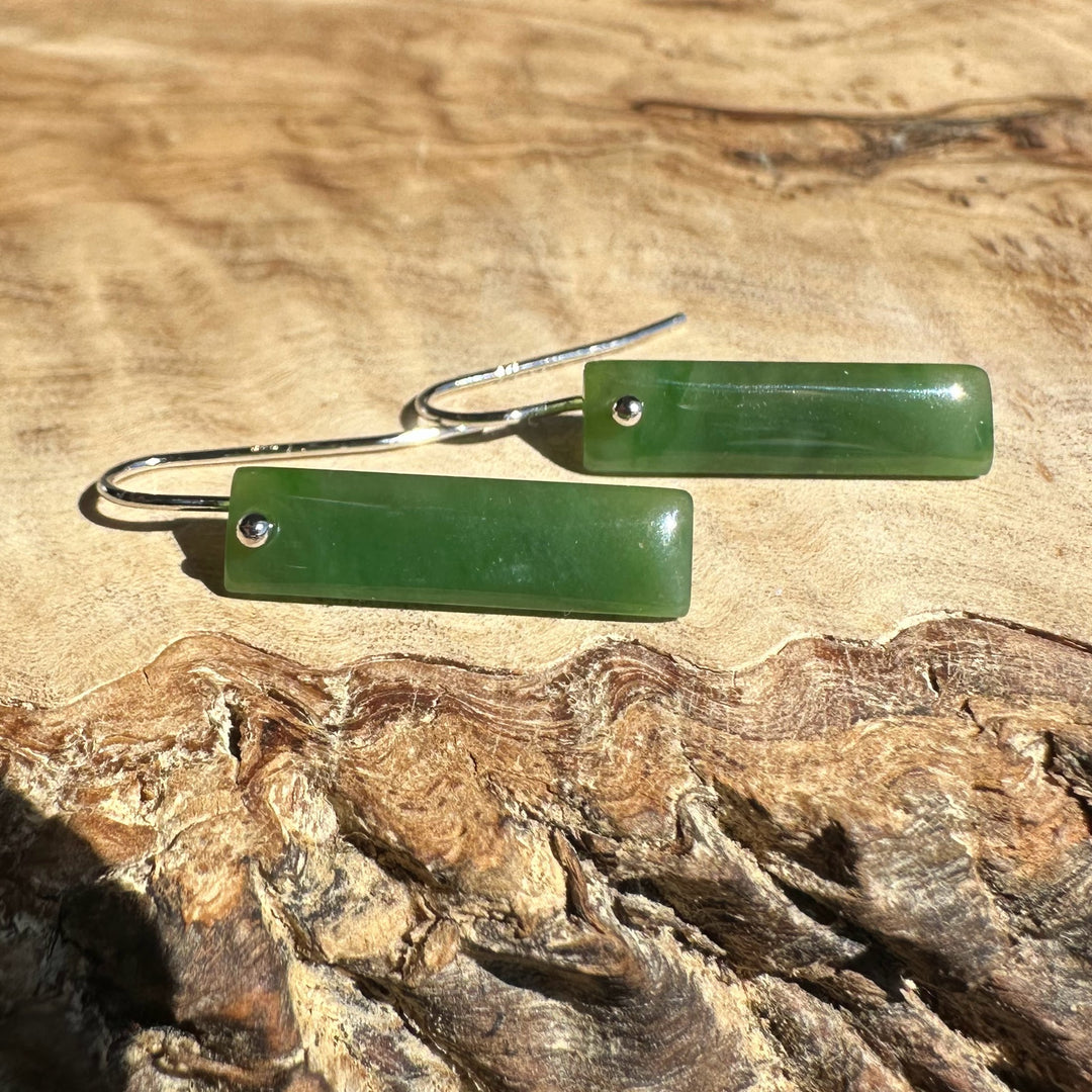 Rectangular green jade bar earrings with silver hooks on a wood surface