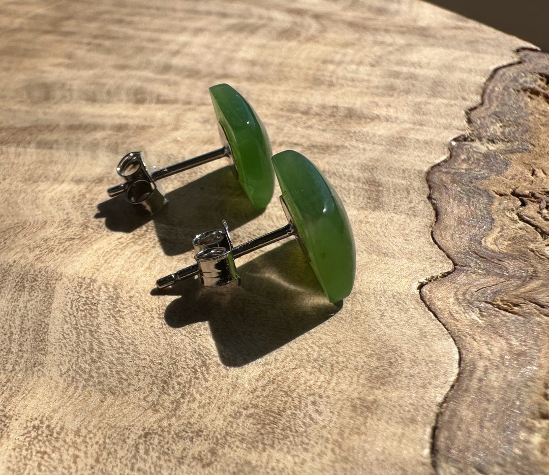 Green jade square stud earrings with silver posts resting on a wooden surface.
