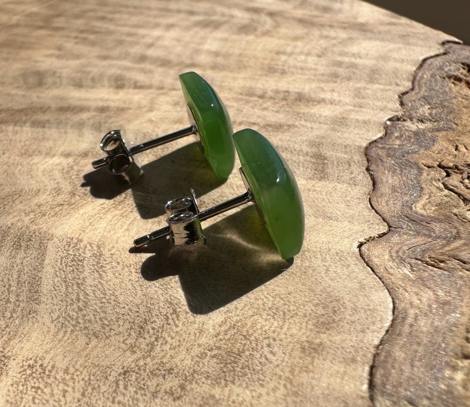 Green jade square stud earrings with silver posts resting on a wooden surface.