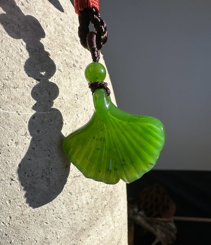 Canadian Jade Ginkgo Leaf Pendant 30mm with green bead on a dark braided cord hanging by a stone pillar