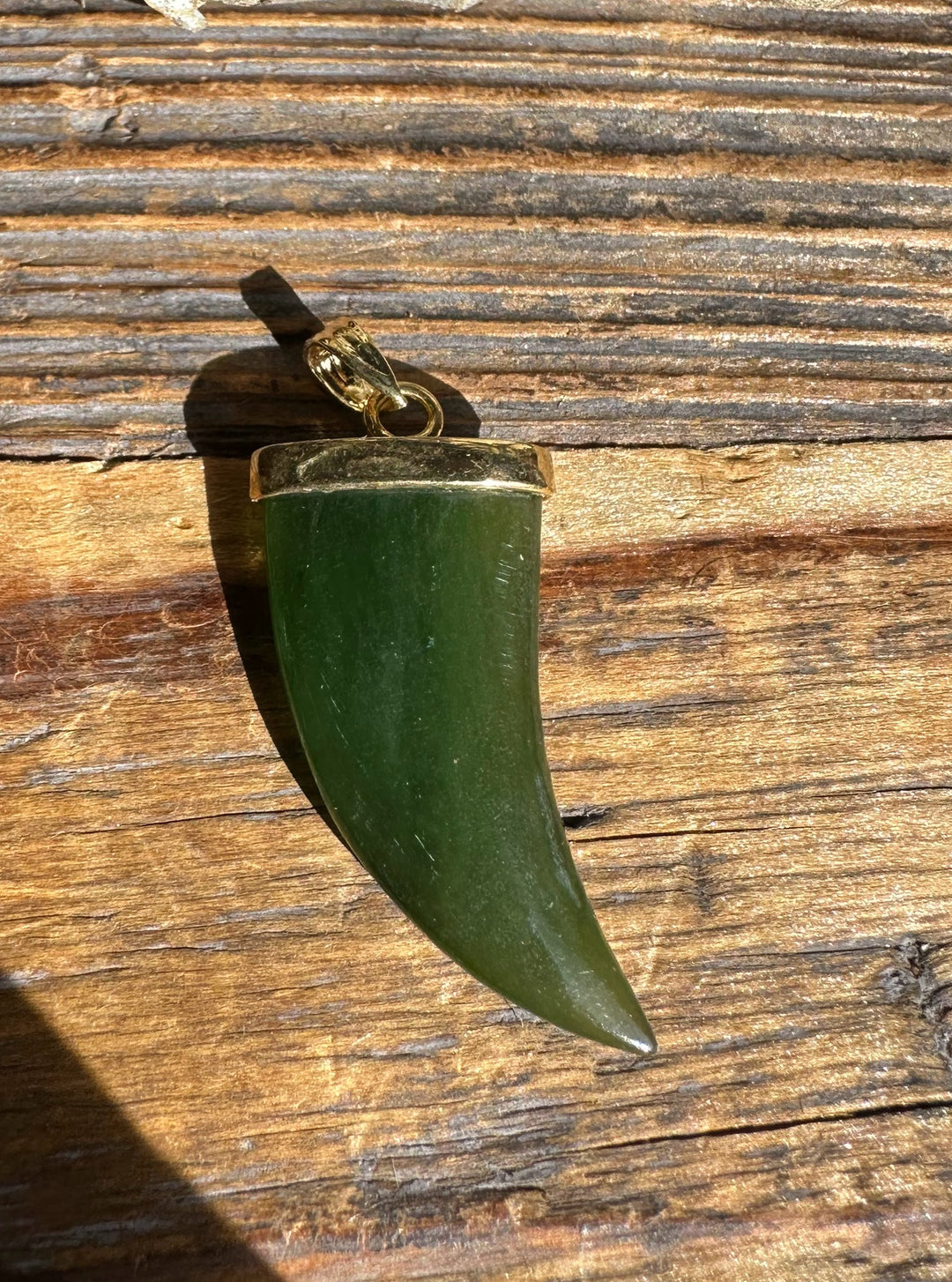 Jade bear claw pendant with gold cap and bail on rustic wood background