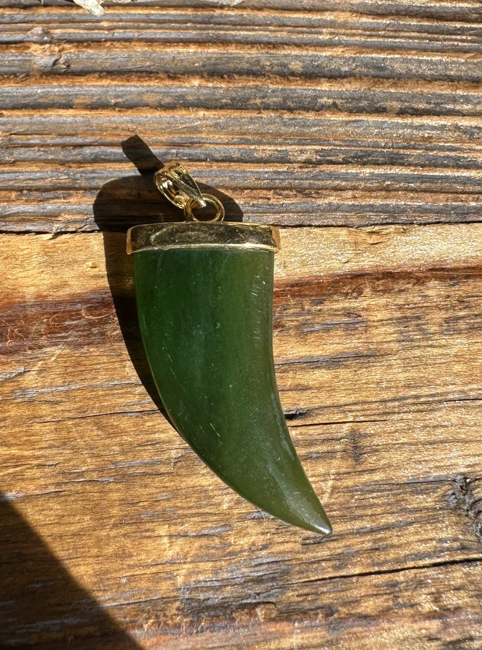 Jade bear claw pendant with gold cap and bail on rustic wood background