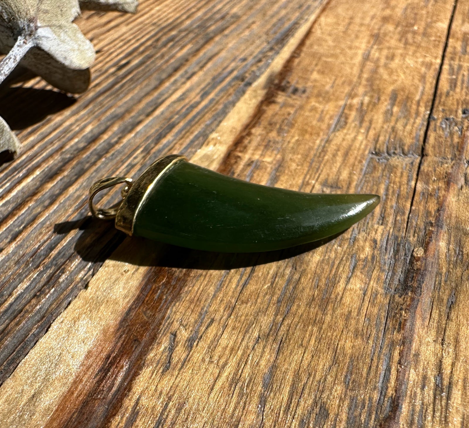 Jade bear claw pendant with gold cap and bail shown in side view on wooden surface