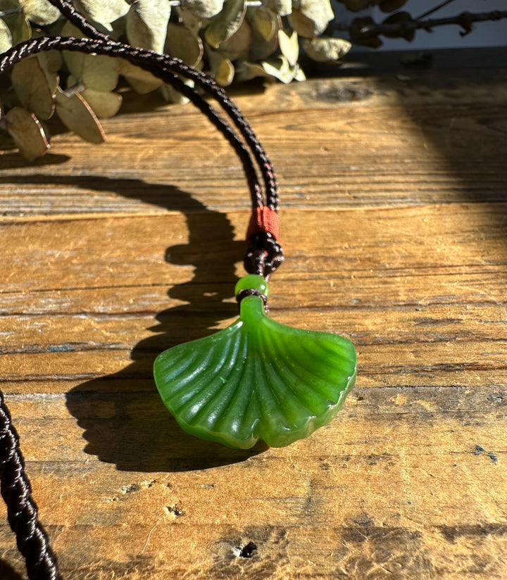 Canadian Jade Ginkgo Leaf Pendant 30mm on a dark braided cord resting on wood