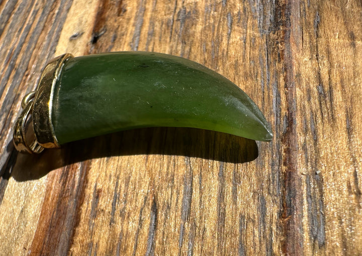 Jade bear claw pendant in profile with gold bail on wood surface