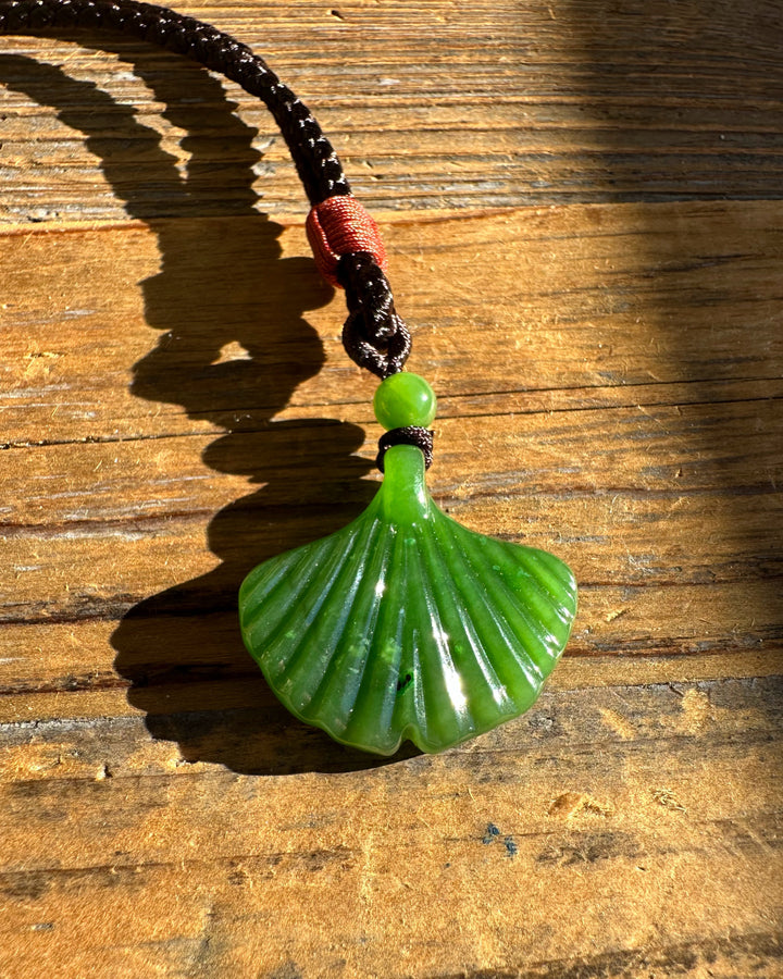 Green jade ginkgo leaf pendant resting on a wooden surface in warm sunlight