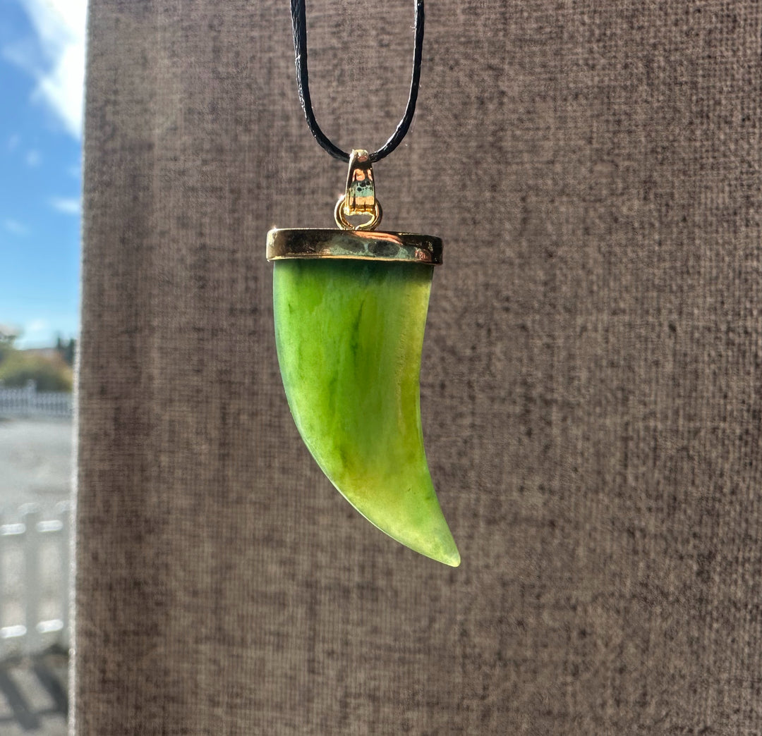 Bright green jade bear claw pendant with gold cap on a black cord against a brown fabric backdrop