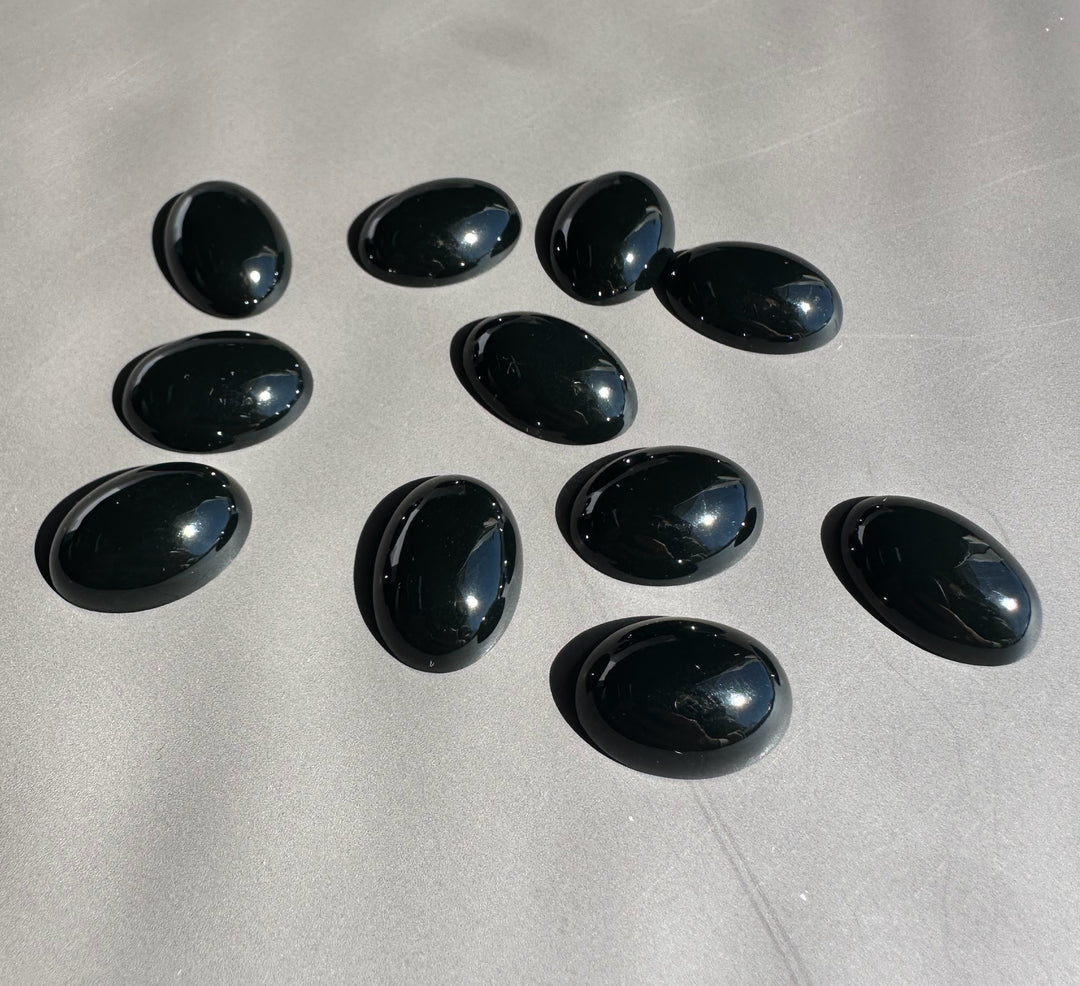 Glossy black oval jade cabochons scattered on a light gray surface.