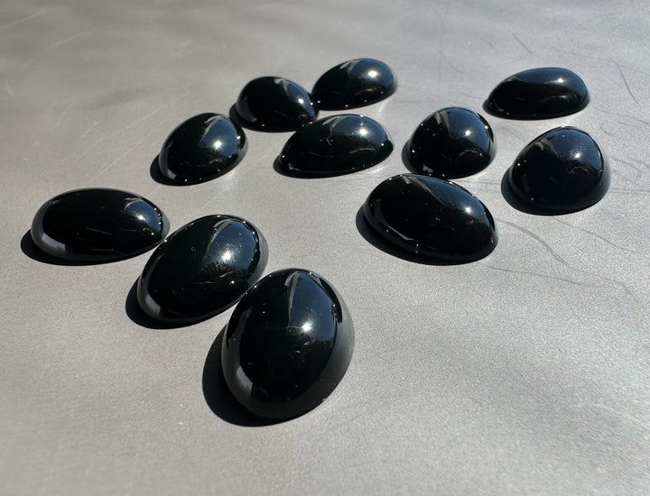 Group of glossy black Wyoming Edwards Jade oval cabochons on a metallic surface