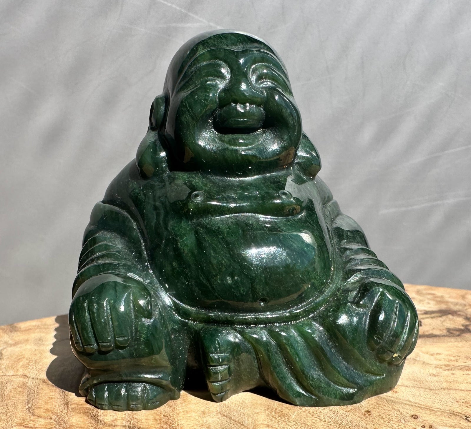 Dark green jade Laughing Buddha statue, 2.5 inches tall, seated on a wooden surface.