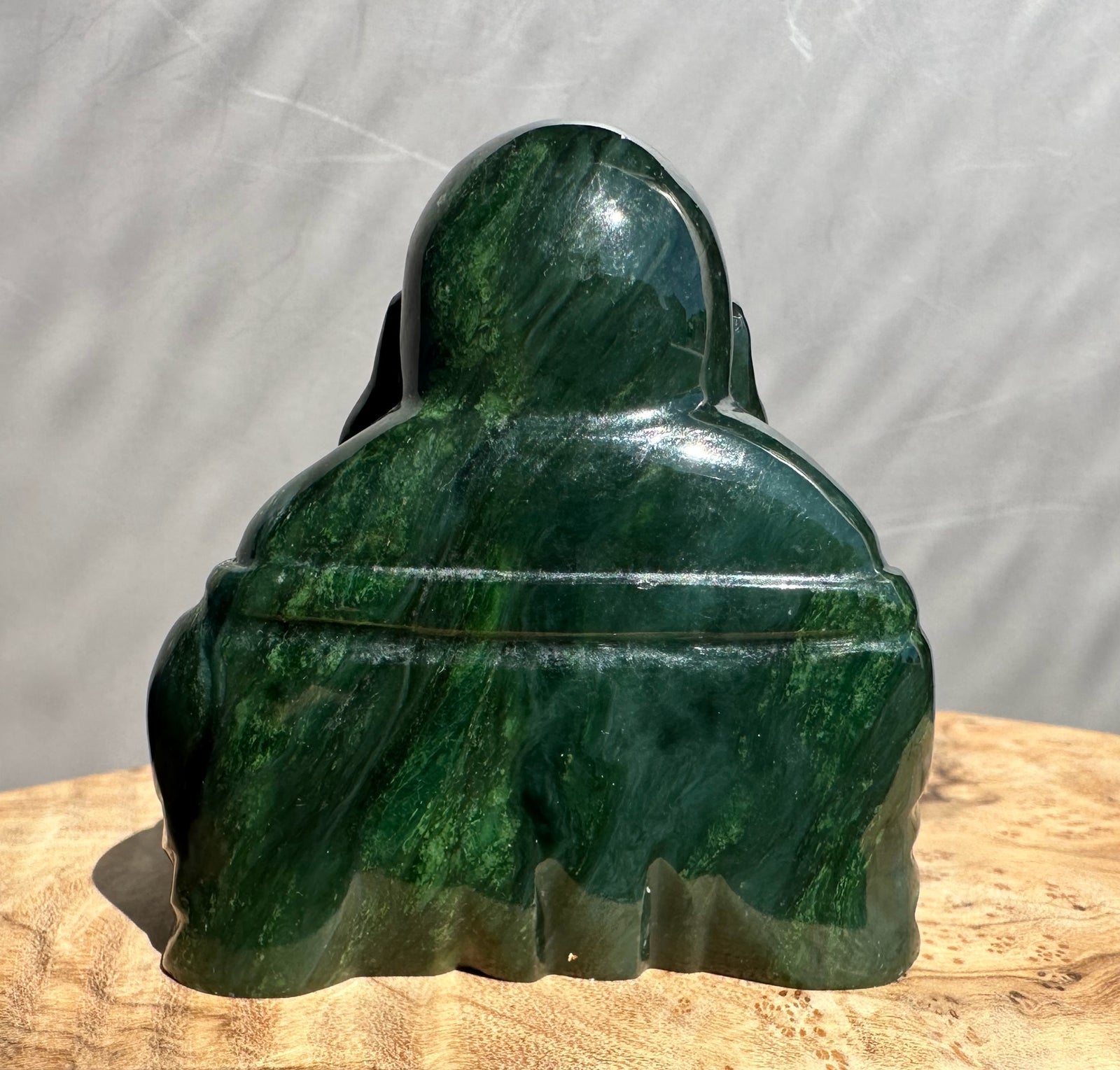 Back view of a 2.5 inch dark green Happy Jade Buddha statue on a wooden surface