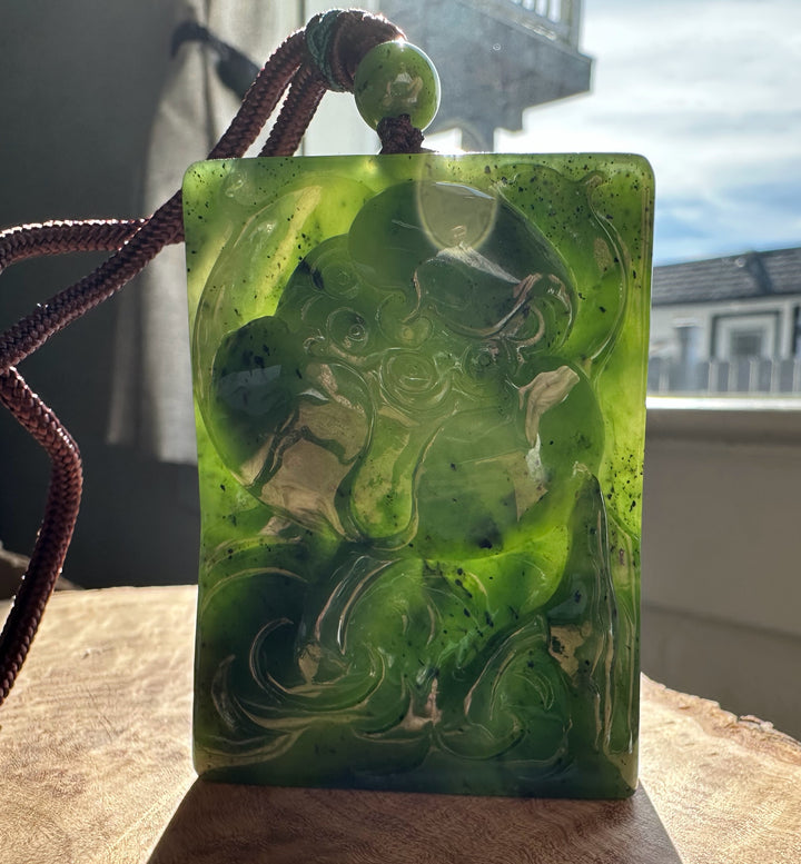 Rectangular green jade pendant with a carved lotus design, hanging from a brown braided cord with a green bead.