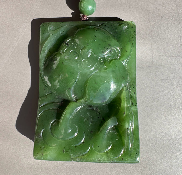 Top view of a vibrant green jade lotus pendant carved into a rectangular slab with a cord and bead at the top.