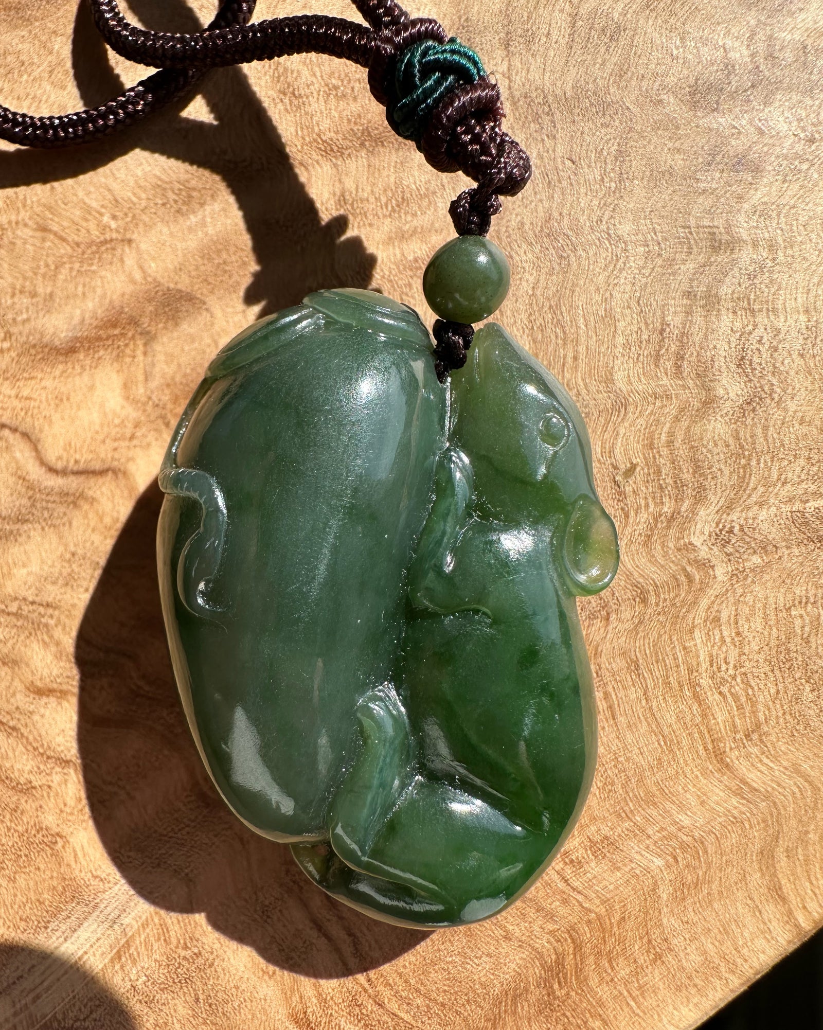 Green jade pendant of a rat on a wooden surface
