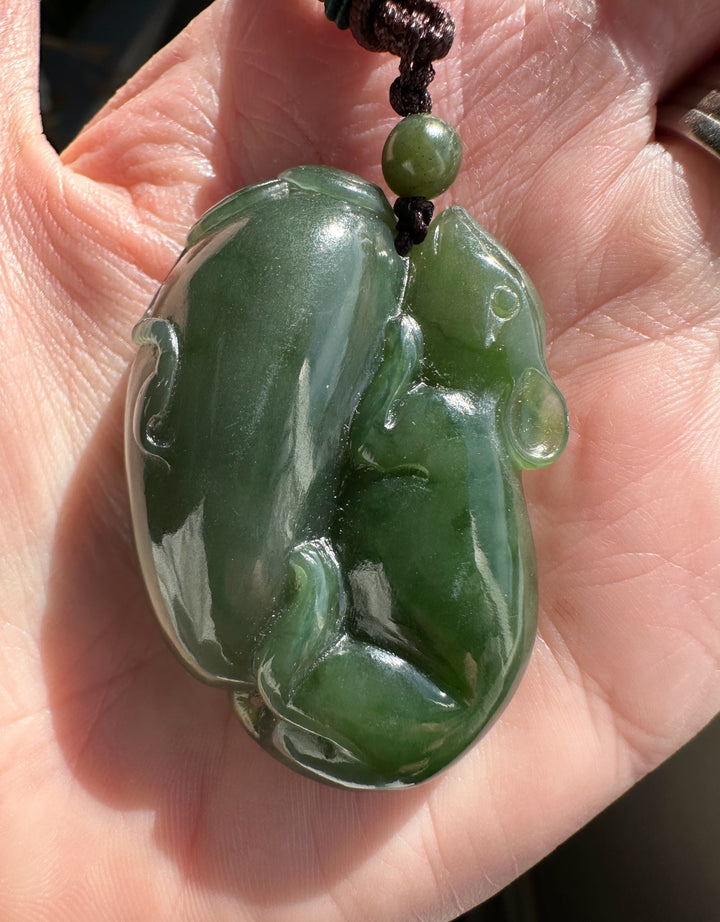 Green jade pendant shaped with a rat and luck held in a hand