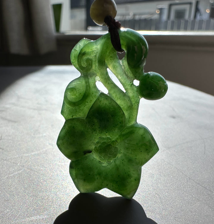 Green jade pendant on a reflective surface with a blurred background