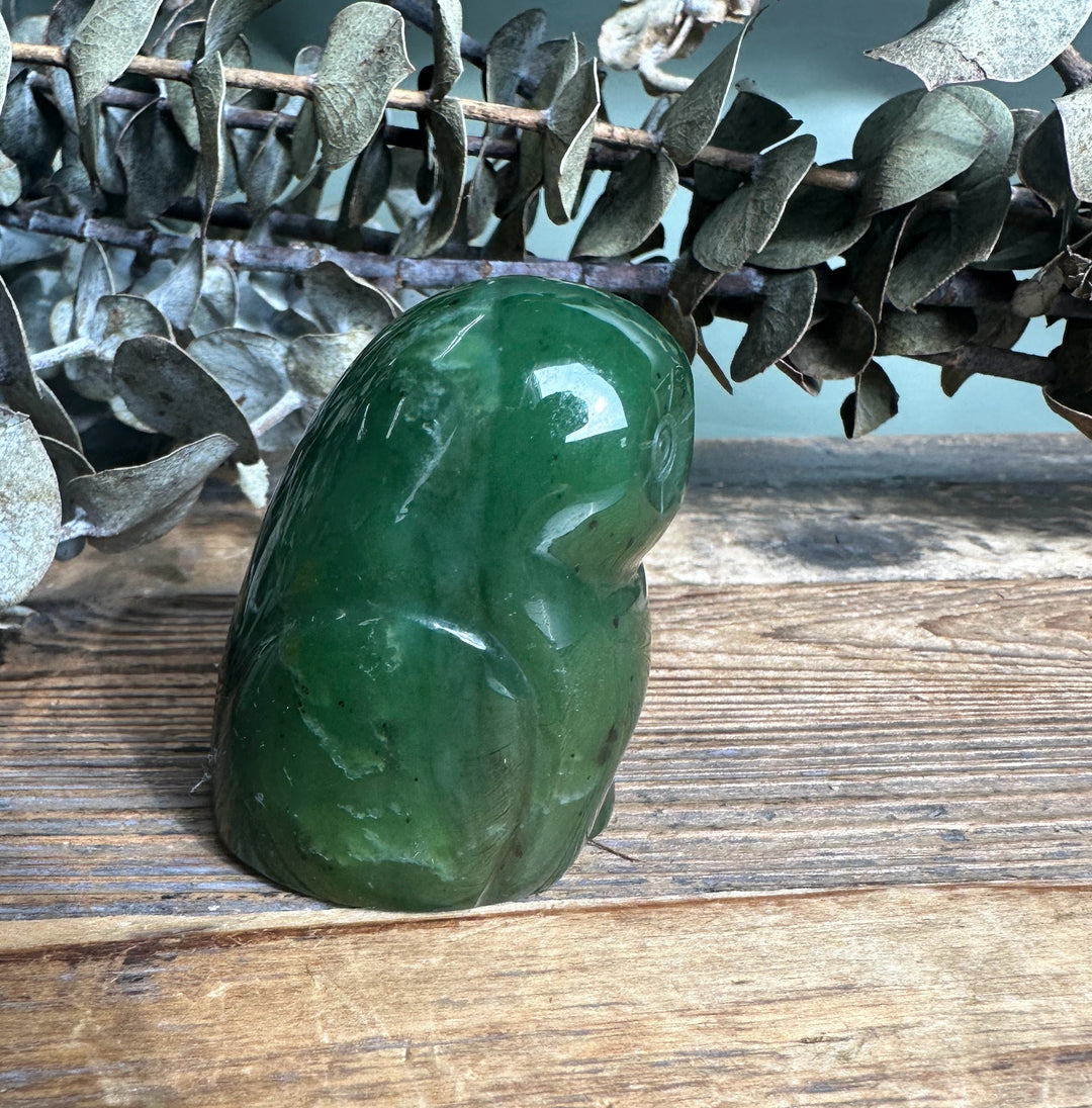 Side view of a glossy green jade owl sculpture resting on a wooden surface.