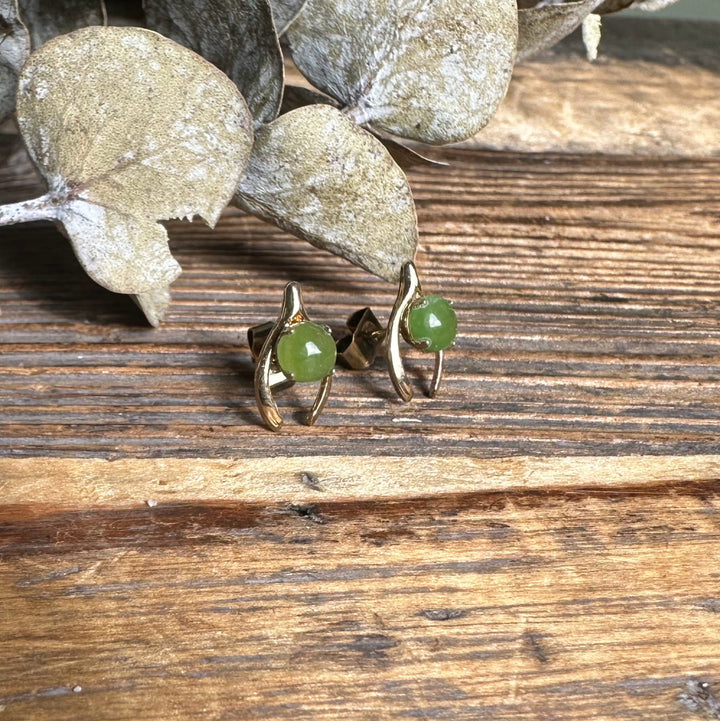 Close up of vintage jade wishbone earrings showing lime green jade cabochons in gold curved settings on wood.