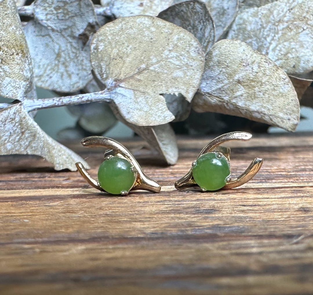 Pair of vintage jade wishbone earrings displayed side by side on weathered wood with green jade cabochons.