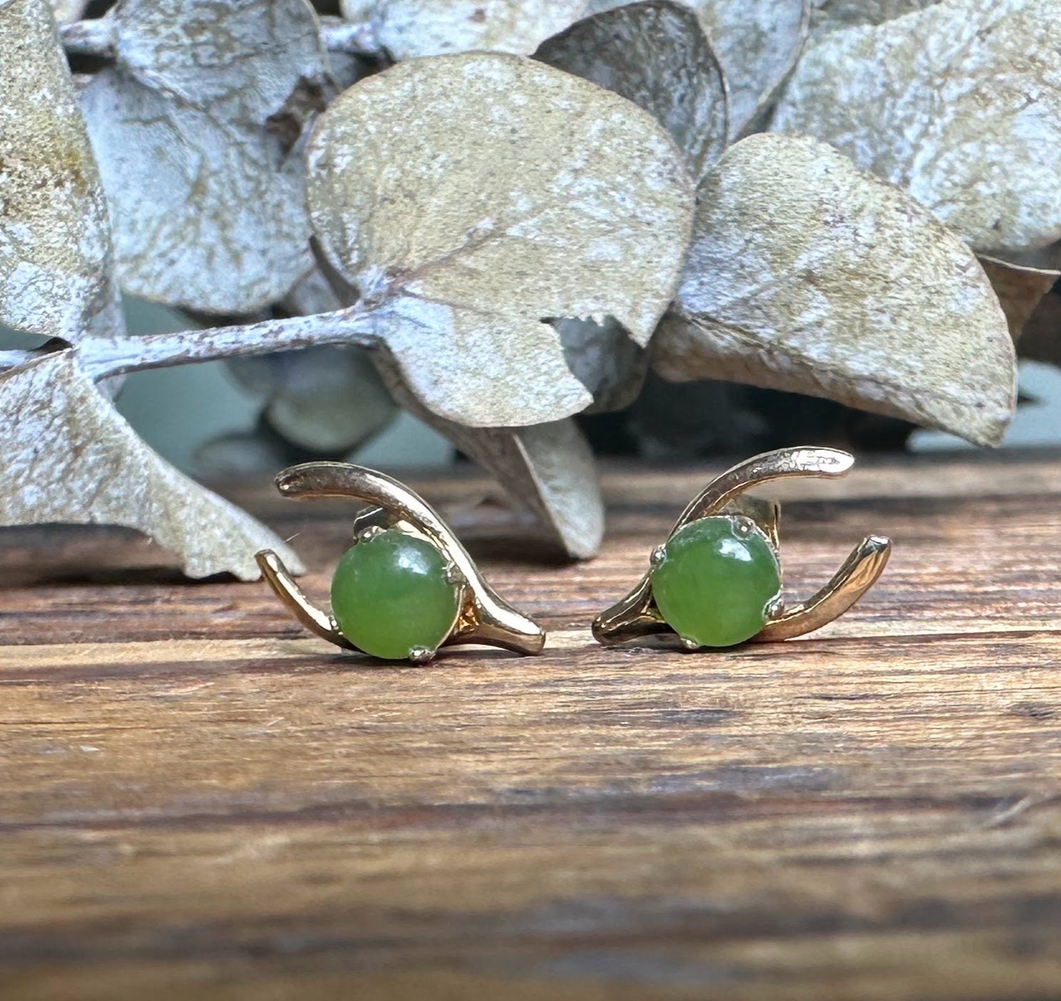 Pair of vintage jade wishbone earrings displayed side by side on weathered wood with green jade cabochons.