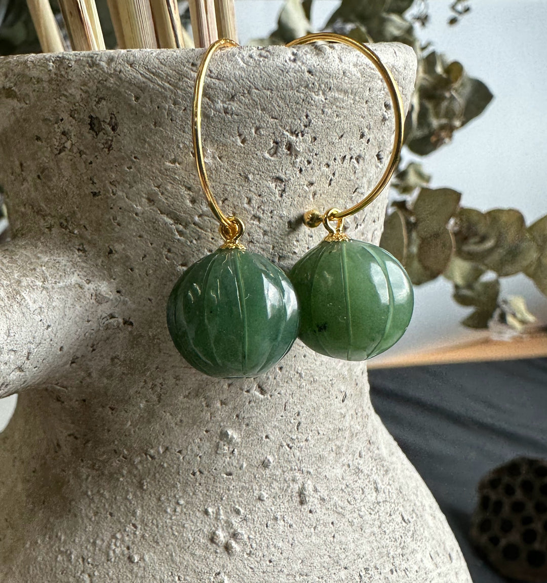 Gold hoop earrings with round Canadian Jade beads hanging from a textured display stand.